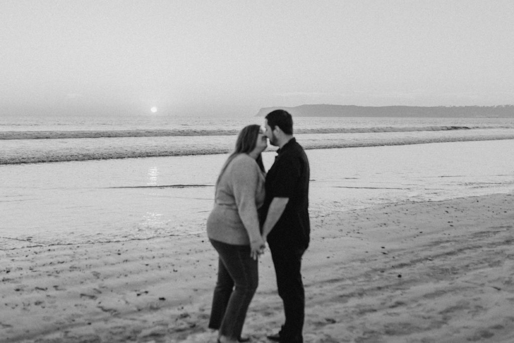 Couple kissing at sunset on Coronado Beach with Point Loma in the background