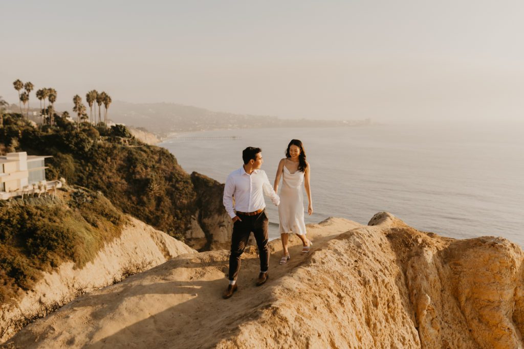 Engaged couple walking along La Jolla cliffside