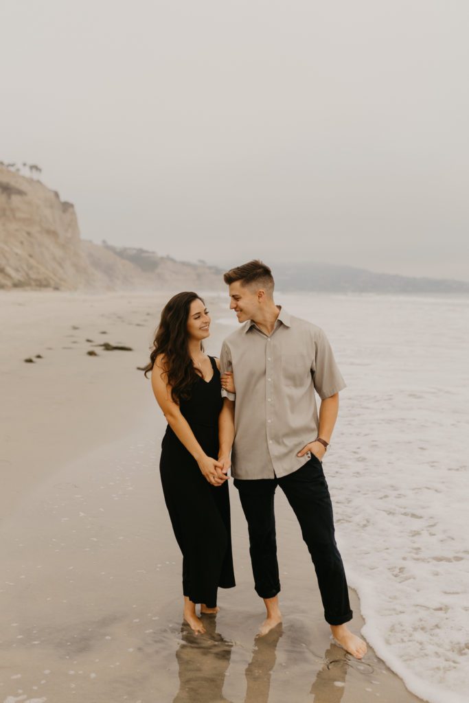 Couple smiling at each other walking along Blacks Beach in San Diego