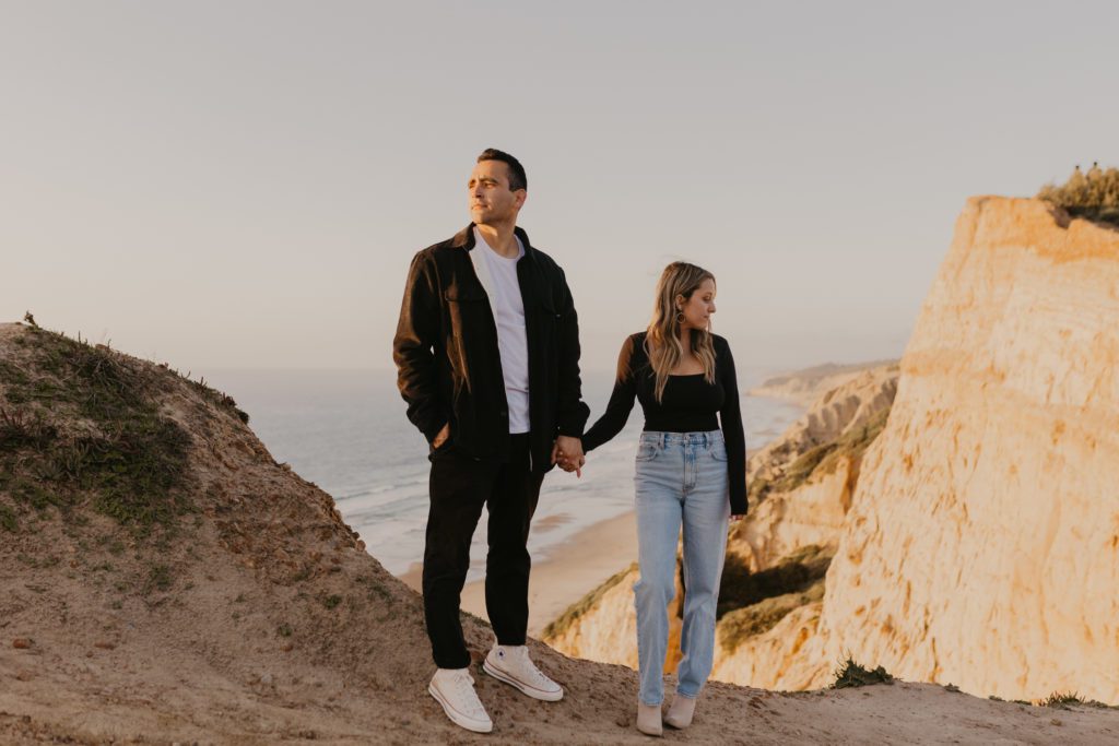 Couple looking away from each other while holding hands atop La Jolla Cliffside