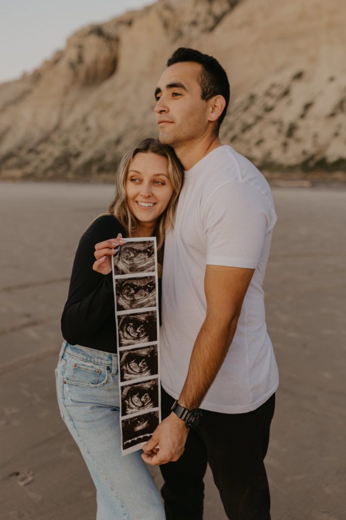 couple smiling away from the camera, holding a pregnancy ultrasound